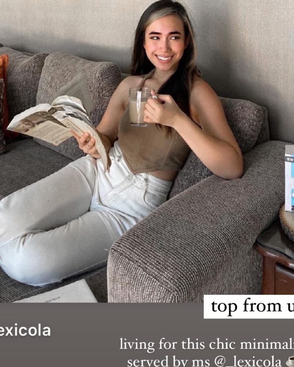 A customer in a tan doce corset top and white jeans, reading on a sofa