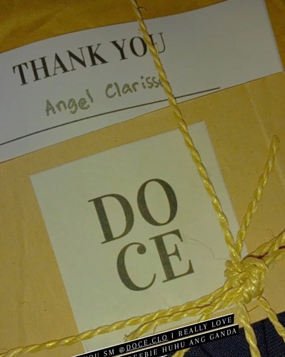 A doce parcel in kraft paper tied with yellow twine, with a DOCE card and a thank-you note addressed by hand to Angel Clarisse